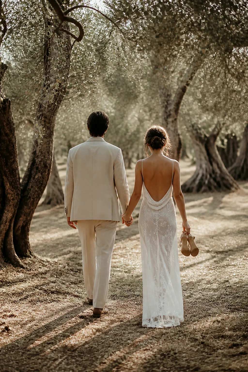 A couple walking hand in hand through an old olive grove