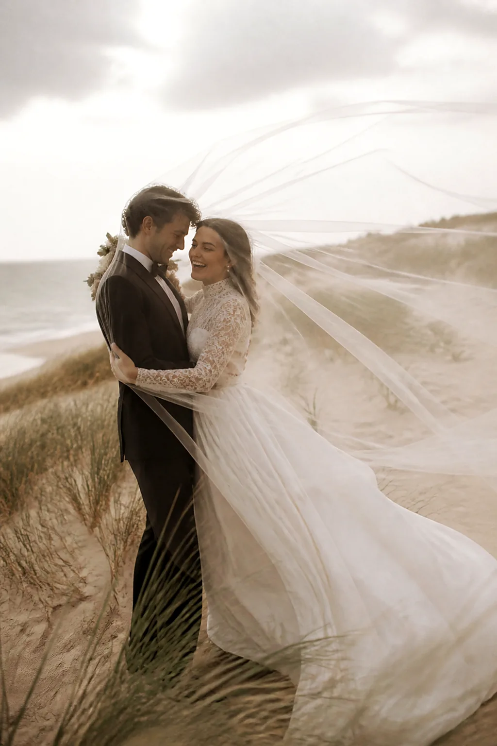 A bride's veil lifting on the wind across pale dunes