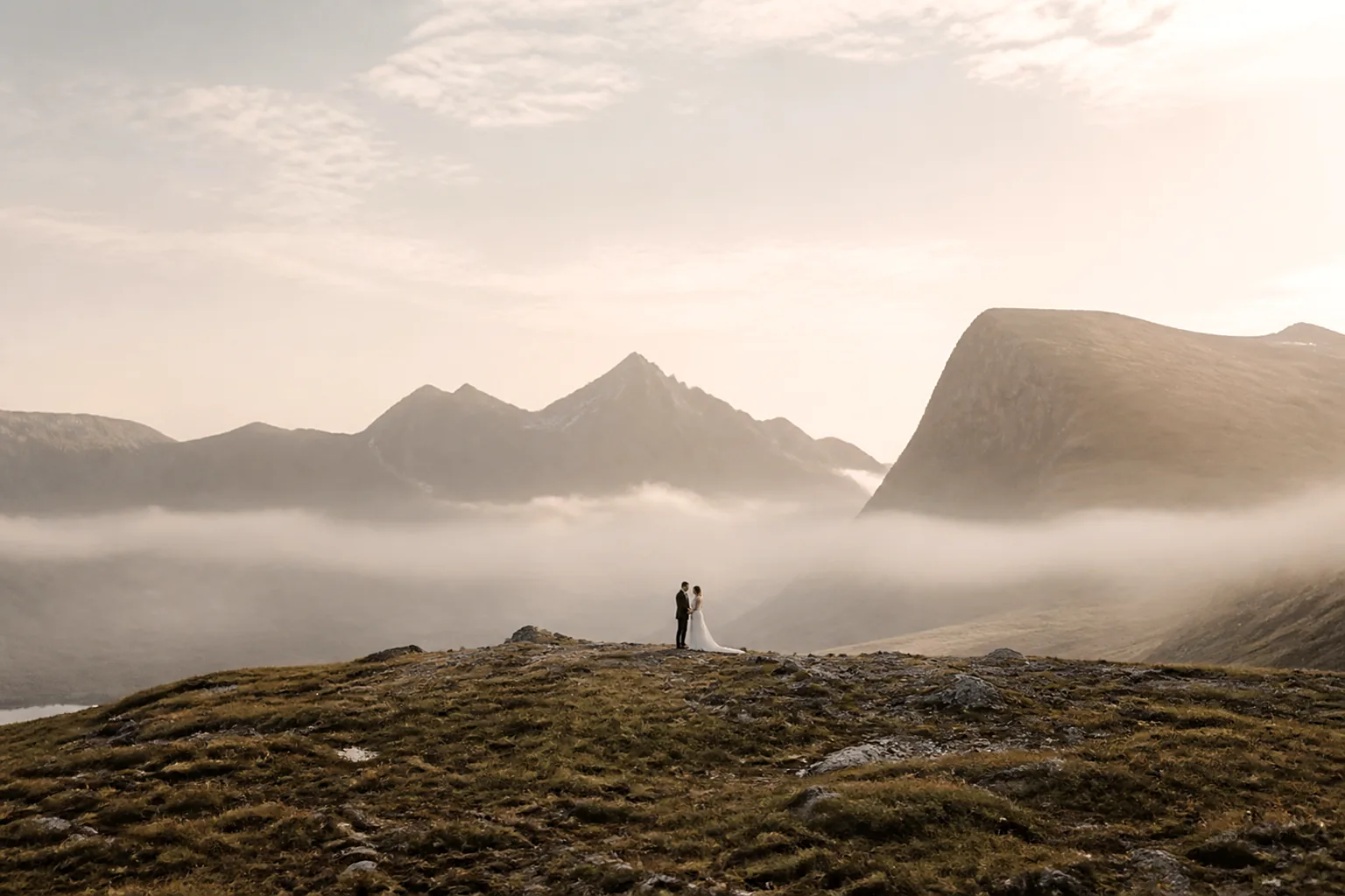An eloping couple standing small in a vast mountain valley at first light
