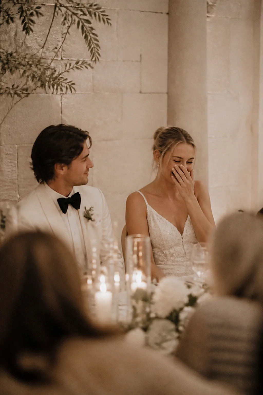 A bride laughing during a speech while the groom watches her